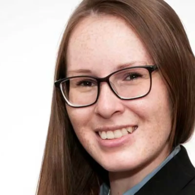 Eine junge Frau mit einer Brille und Sommersprossen posiert vor einem weißen Hintergrund.