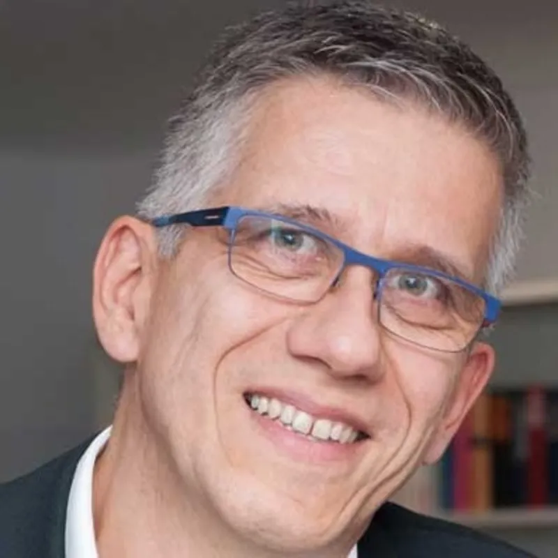 Ein Mann im Buero traegt ein Anzug und eine blaue Brille