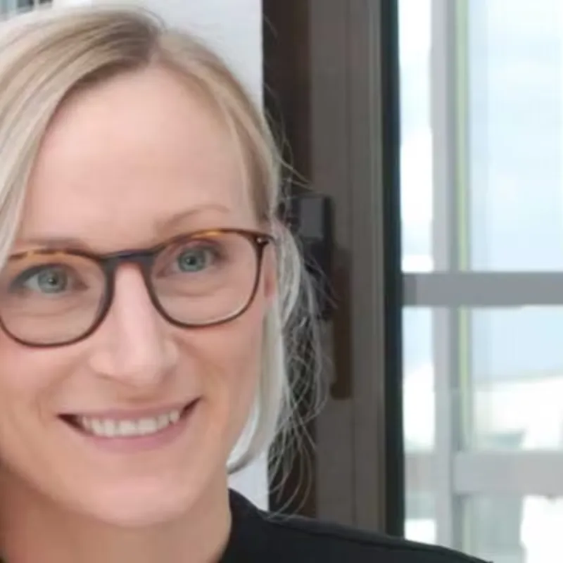 Eine Frau mir blonden Haaren und einer runden Brille sitzt im Buero.
