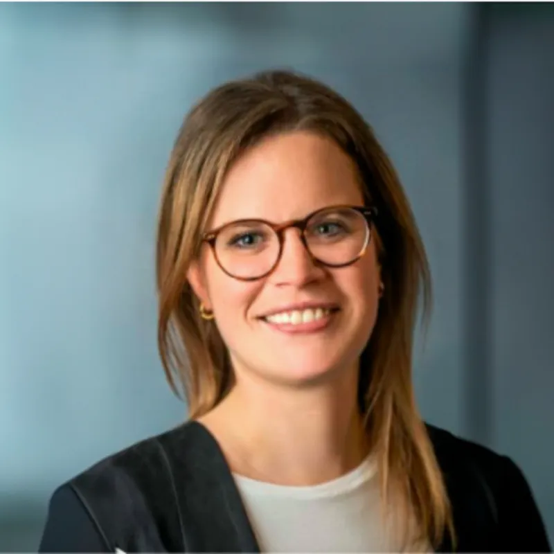 Eine Frau mit Brille steht laechelnd vor einem blauen Hintergrund