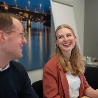Zwei Personen lachen gemeinsam in einem Konferenzraum. 